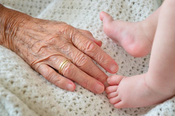 an elderly person's hand touches a baby's foot