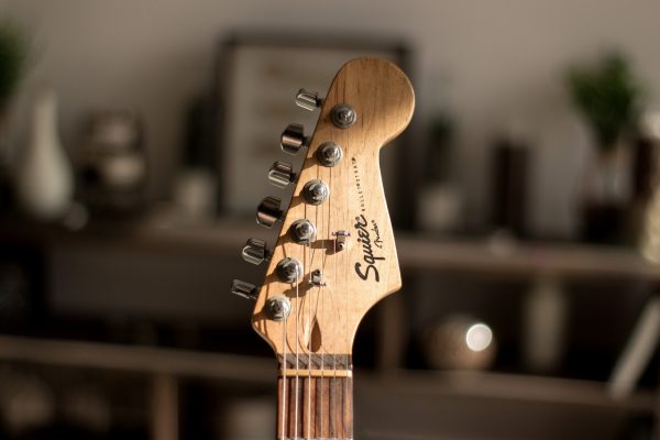 Close-up of a Squier electric guitar headstock with tuning pegs, blurred background.