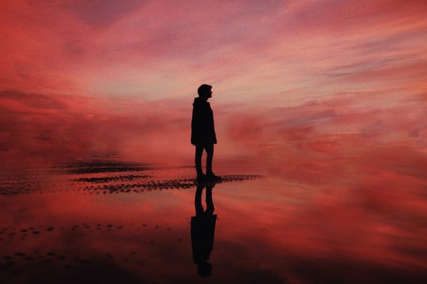 person standing in silhouette at the shore against a bright pink and red sky