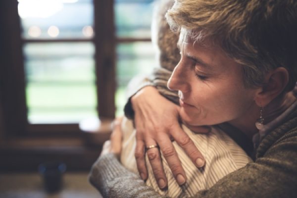 Two people hugging warmly near a window, with soft lighting enhancing the peaceful atmosphere.