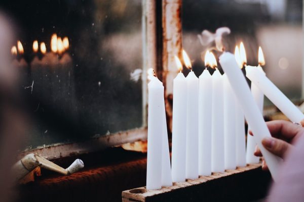 lighting all white hanukkah candles in window with reflection of candles