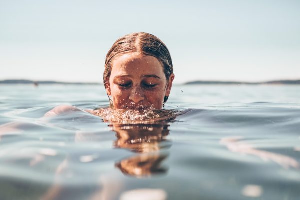 white woman with eyes closed immersed in water, half her face submerged, smiling