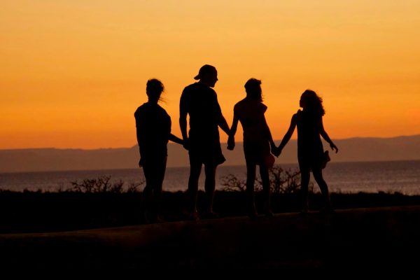 Silhouette of a family holding hands and walking at sunset near the ocean.