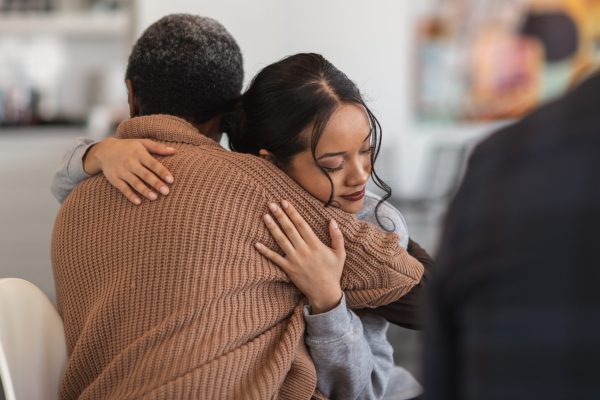 Two people hug each other closely, offering comfort and emotional support in an indoor setting.