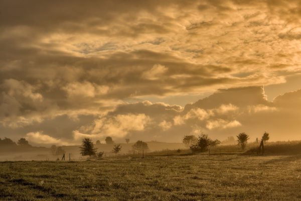 a field with clouds waving across the sky above it