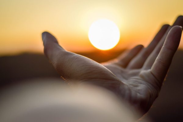 open hand in the foreground, sun setting in the background