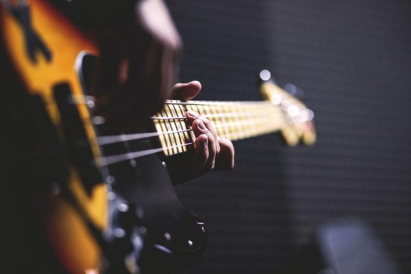 Close-up of a person playing an electric bass guitar with a blurred soundproof room background.