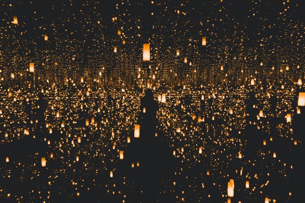 Silhouette of a person surrounded by countless glowing lanterns in a dark, reflective room.