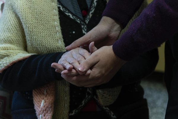 closeup of elderly woman's hands being held by younger person's hands, both light-skinned