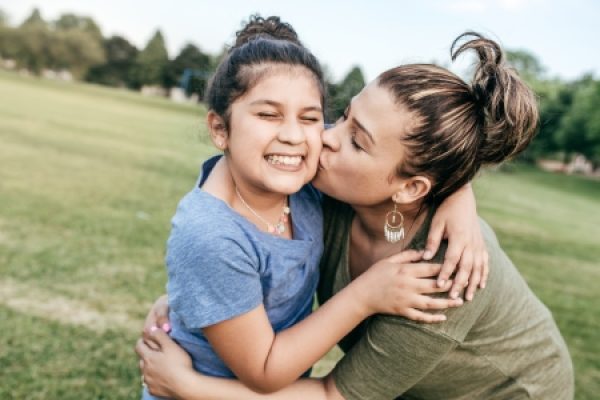 A woman kisses a smiling girl on the cheek in a grassy field.