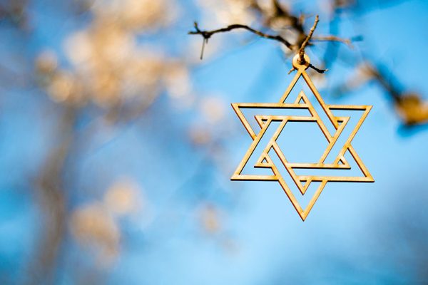 Gold star of david hanging from branch against blue sky