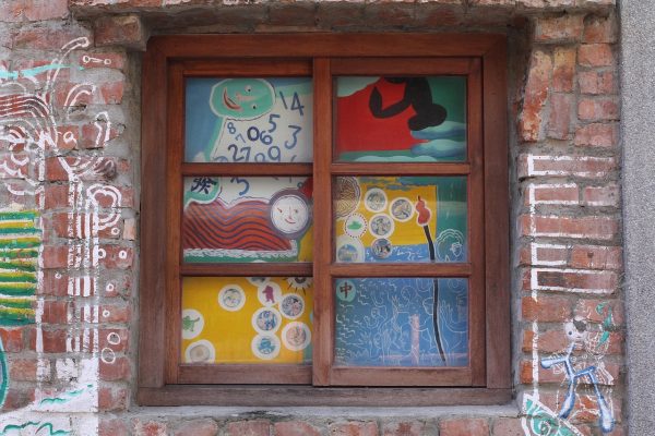 A brick wall window with colorful, whimsical art and abstract drawings on the glass panes and surrounding bricks.