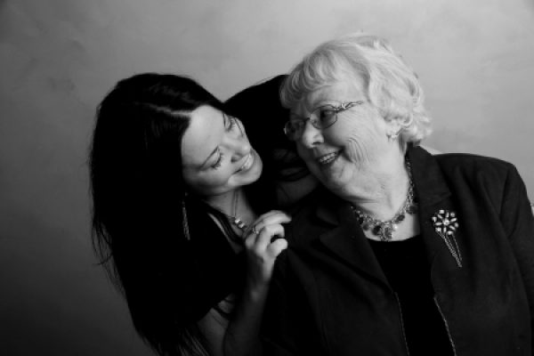 Black and white photo of a young woman embracing an elderly woman, both smiling warmly at each other.