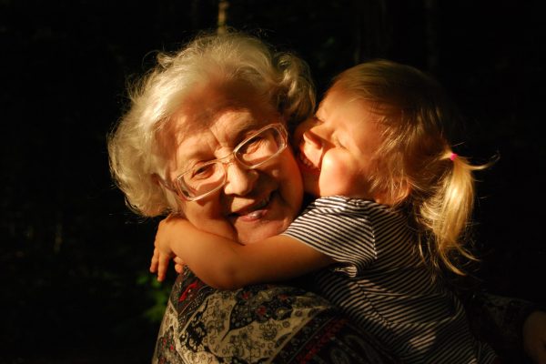 Smiling grandmother being hugged by toddler in pigtails against a black background