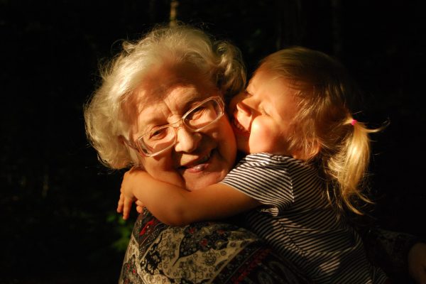 Smiling grandmother being hugged by toddler in pigtails against a black background