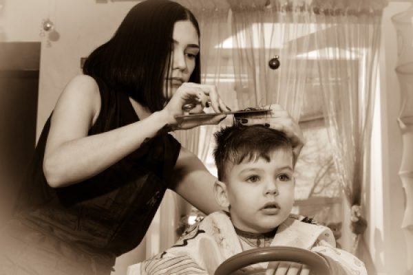 A woman giving a haircut to a young boy sitting in a salon chair.