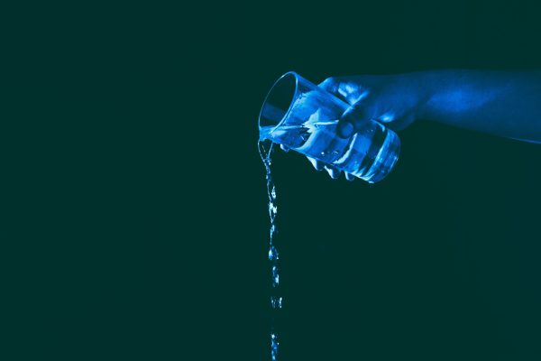 hand pouring water from a glass lit by blue light