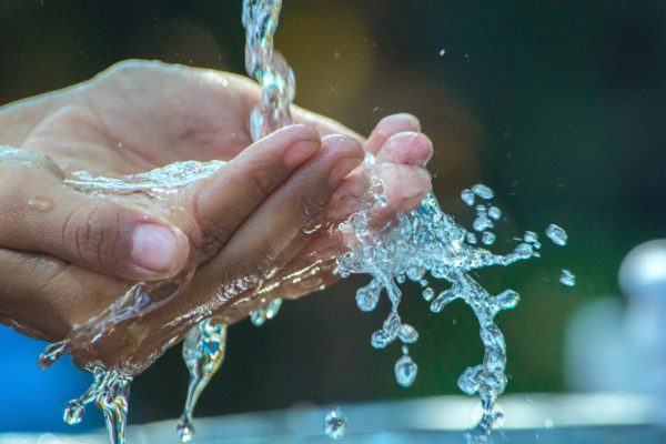 Hands cupping flowing water, with splashes reflecting sunlight.