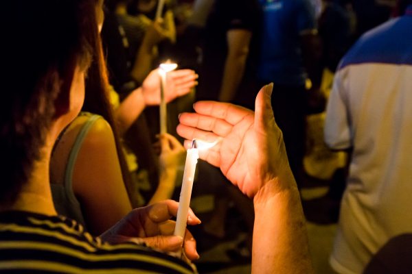 People holding lit candles at a nighttime vigil or gathering.