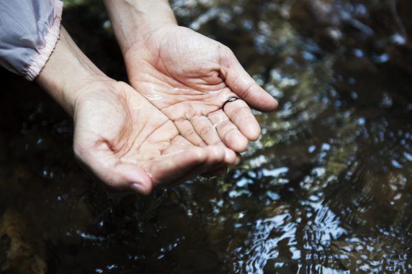 white hands cupping water over a body of water