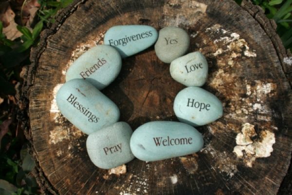 Smooth stones with words like Friends, Love, and Hope arranged on a tree stump.