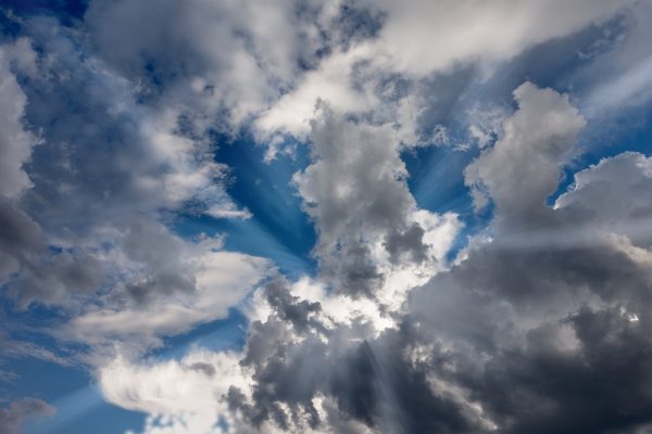 Dramatic sky with sunbeams breaking through fluffy, dark clouds against a vibrant blue backdrop.