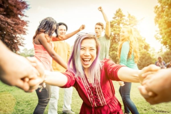 A group of diverse people holding hands and smiling outdoors on a sunny day.
