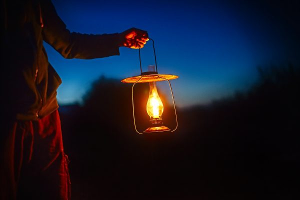 Person holding a glowing lantern outdoors at dusk, with a blue and orange sky in the background.
