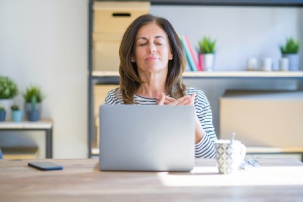 a person with medium length hair with a laptop in front of them closes their eyes and covers their heart with their hands