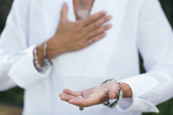 A person in a white shirt holds a small object in one hand while touching their chest with the other.