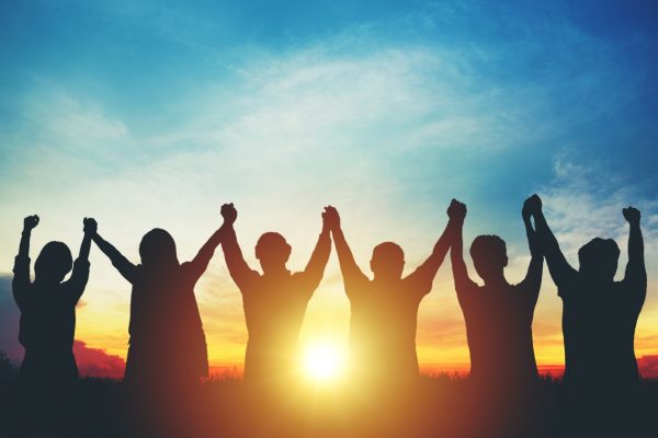 Silhouetted group of people holding hands together against a sunset sky.
