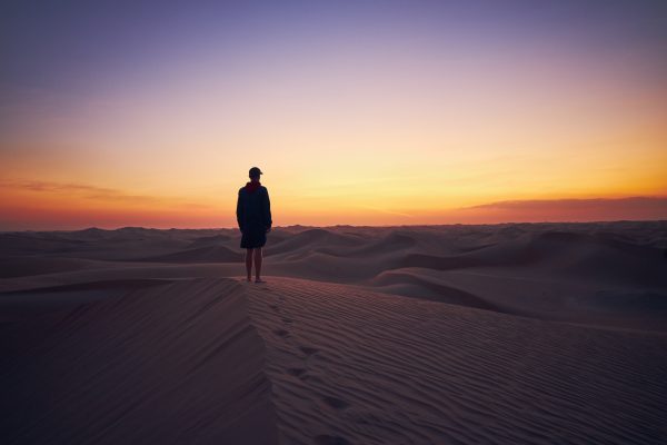person shown far away in silhouette against a sky in which the sun has set and the sky is blue yellow and orange