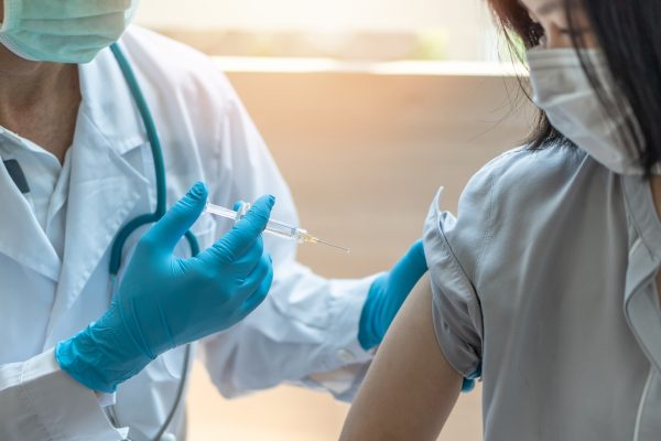 Doctor administering a vaccine to a woman wearing a mask.
