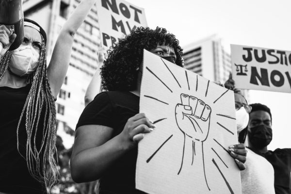 Protesters hold signs with messages, including a fist symbol and Justice Now, during a demonstration.