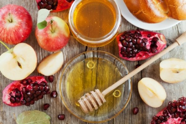 an assortment of apples, pomegranates, and bowls of honey