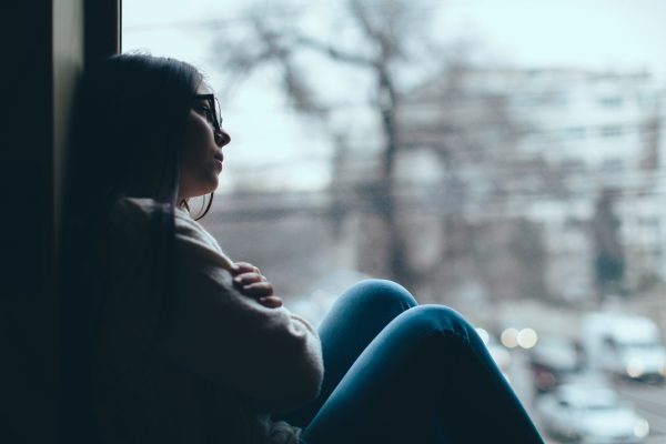 A person sits by a window with arms crossed, looking outside.