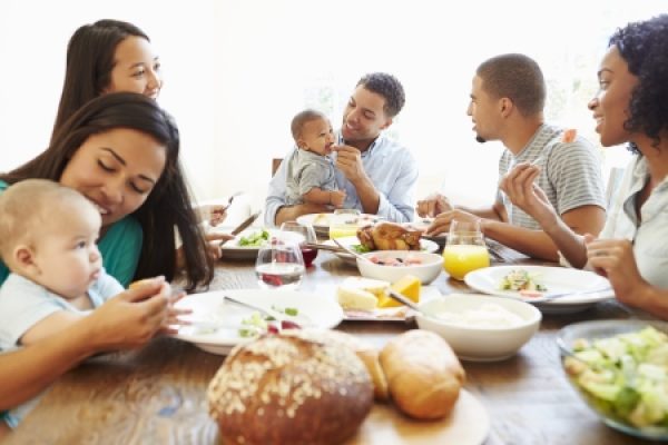 A group of people enjoying a meal together around a dining table, with two babies present.