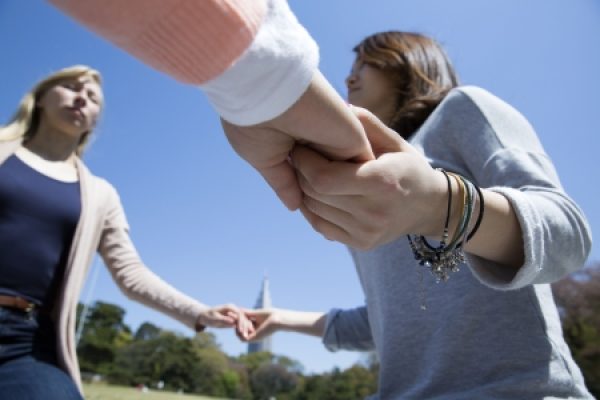 Three people holding hands outside on a sunny day, with a clear blue sky and trees in the background.