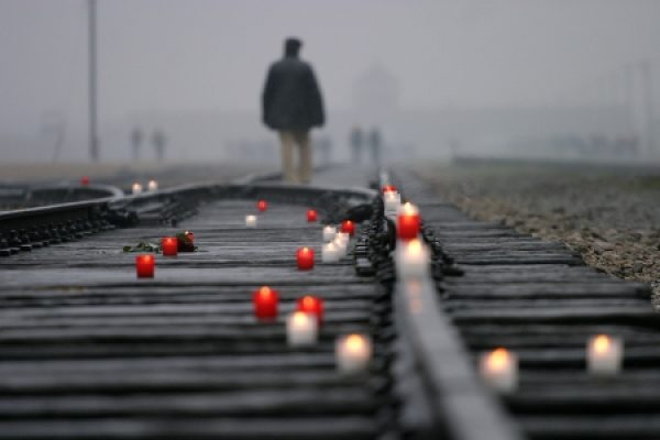 Candles on train tracks in foggy weather, with a solitary person walking in the distance.