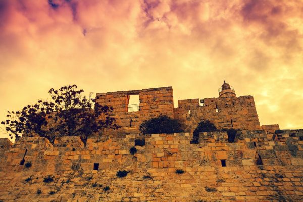 Ancient stone castle with a tower, silhouetted against a dramatic, colorful sunset sky.