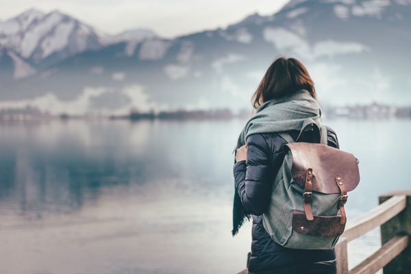 woman with backpack facing a wintry lake and mountains