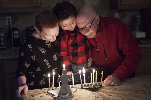 Family lighting menorah candles together, smiling in a cozy kitchen setting.