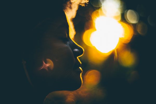 Silhouette of a person against a bright, blurred sunset background with a lens flare effect.