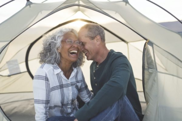 Older couple laughing together inside a tent, enjoying a sunny day outdoors.