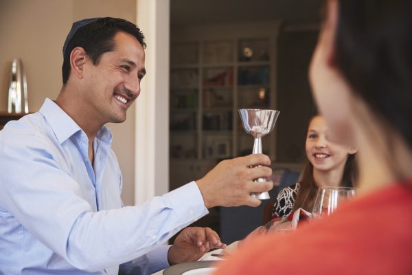 Man holding a goblet, smiling at a young girl at a dining table. A woman is partially visible in the foreground.