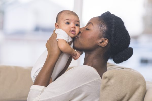 A woman holding and kissing a baby indoors on a couch.