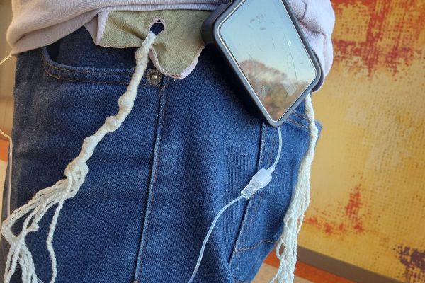 A person wearing jeans with an insulin pump tucked into a pocket, connected to a charger with braided strings.