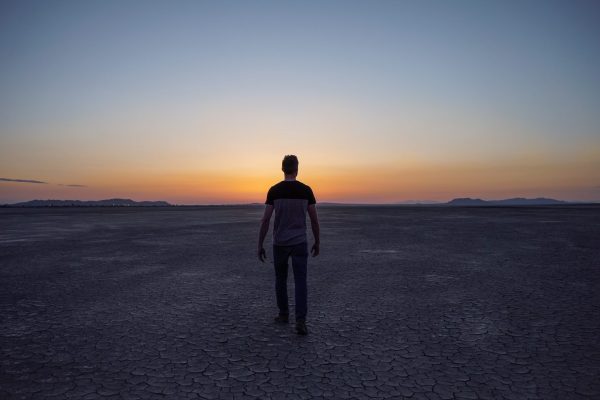 silhouette of person walking in desert toward sunset