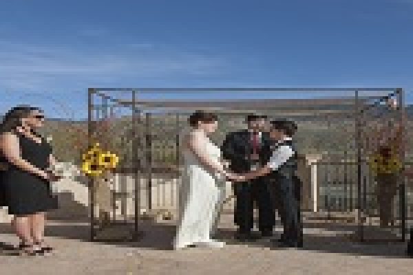 A couple holding hands during an outdoor wedding ceremony with bridesmaids and a scenic backdrop.