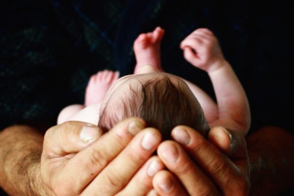 Hands gently cradling a newborn babys head, viewed from above.